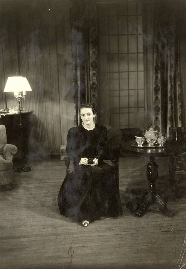 During the drama production of 'Dangerous Corner,' a women sits in a chair with a tea cup. Cast: Robert Herrick as Gordon Whitehouse, Dorothy Pierce as Freda Chatfield, Eldred Stephenson as Robert Chatfield, Alline King as Olwen Peel, Paul Selby as Charles Stanton, Nina Varian as Betty Whitehouse, Ethlyn O'Neal as Maud Mockridge
