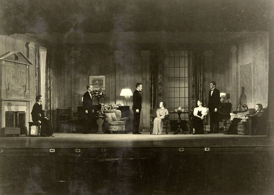 The truth party at the Chatfield home, during the drama production of 'Dangerous Corner.' Men stand on stage as the women sit. Cast: Robert Herrick as Gordon Whitehouse, Dorothy Pierce as Freda Chatfield, Eldred Stephenson as Robert Chatfield, Alline King as Olwen Peel, Paul Selby as Charles Stanton, Nina Varian as Betty Whitehouse, Ethlyn O'Neal as Maud Mockridge