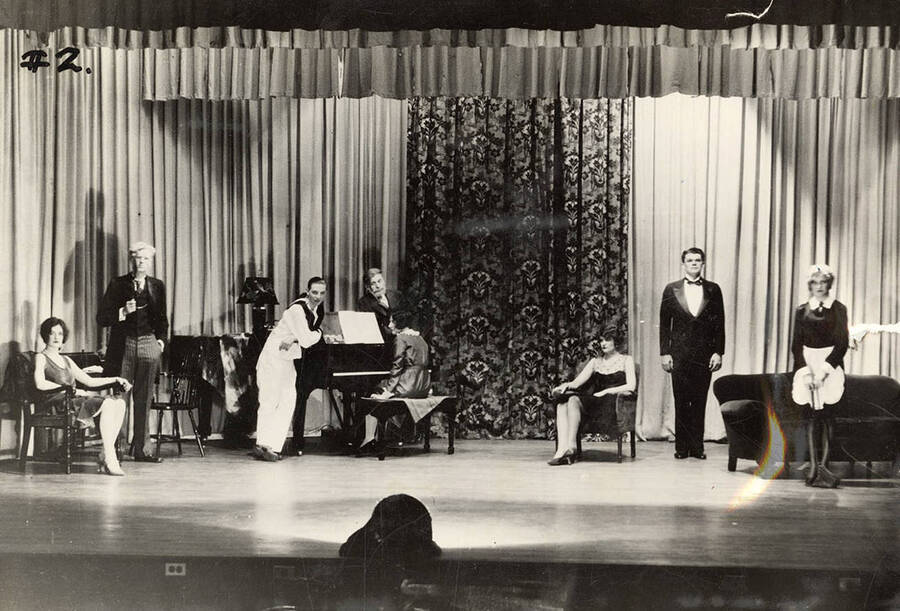 Men and women hang out around a piano as a woman plays during the drama production of 'Fourteen,' written by Talbot Jennings