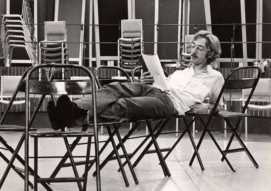 A man lays across some chairs, reading his lines, during the drama production of 'You're a Good Man, Charlie Brown.'