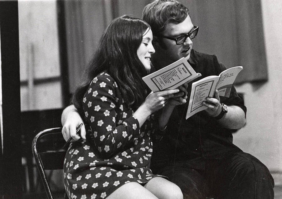 A man and woman sit close, reading through their lines during a drama production.