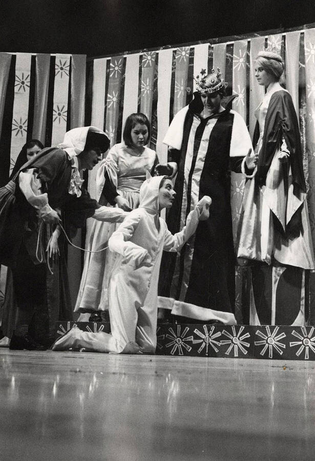 Men and women stand around looking at a faux cat onstage during the drama production 'The Pale Pink Dragon.'