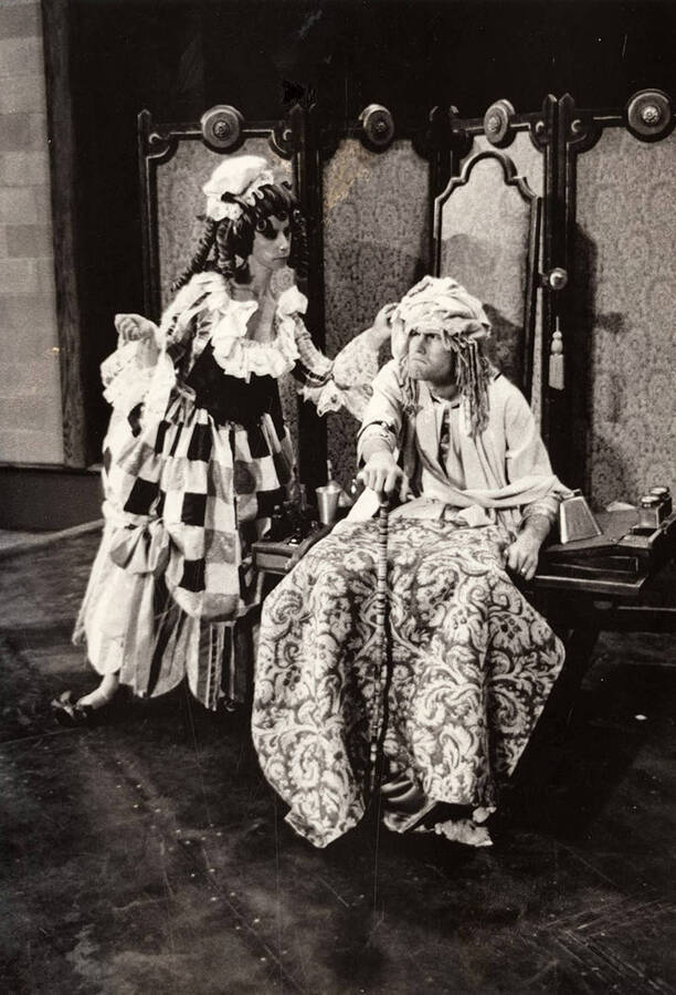 An angry-looking man sits in a chair as a woman stands next to him during a drama production of "The Imaginary Invalid" in the Hartung Performing Arts Center.