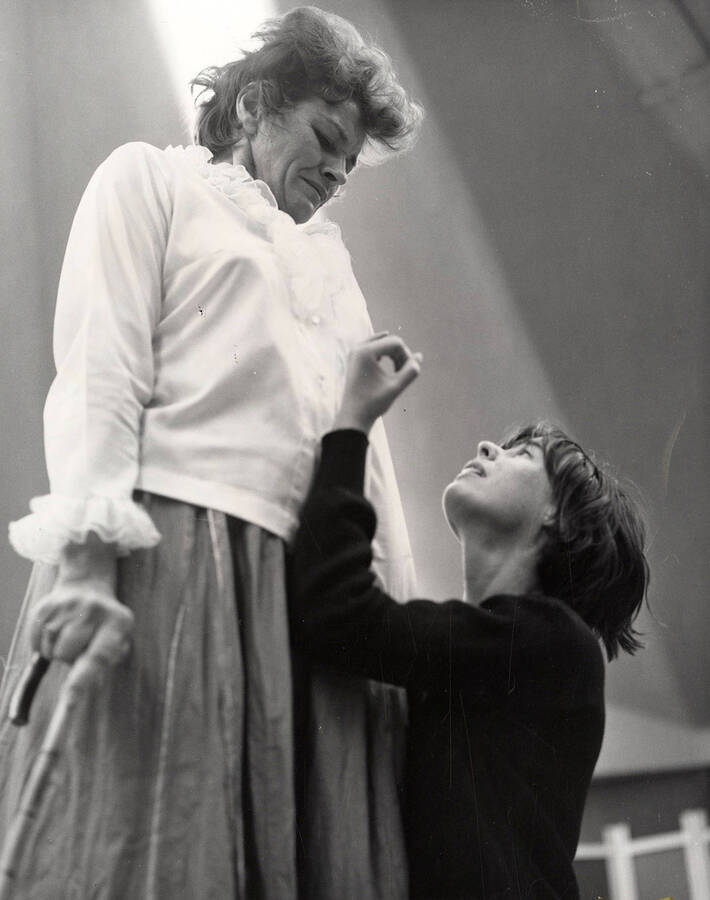 A woman looks down at another woman who is kneeling during a drama production.