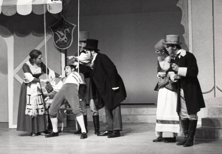 A woman helps a man out of a chair as others look on during a drama production.