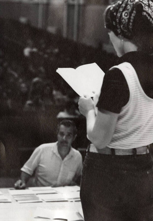 A women reads lines in front of a large audience during a drama production.