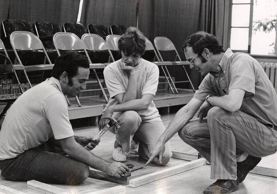 Two men and a woman build set pieces during a drama production.