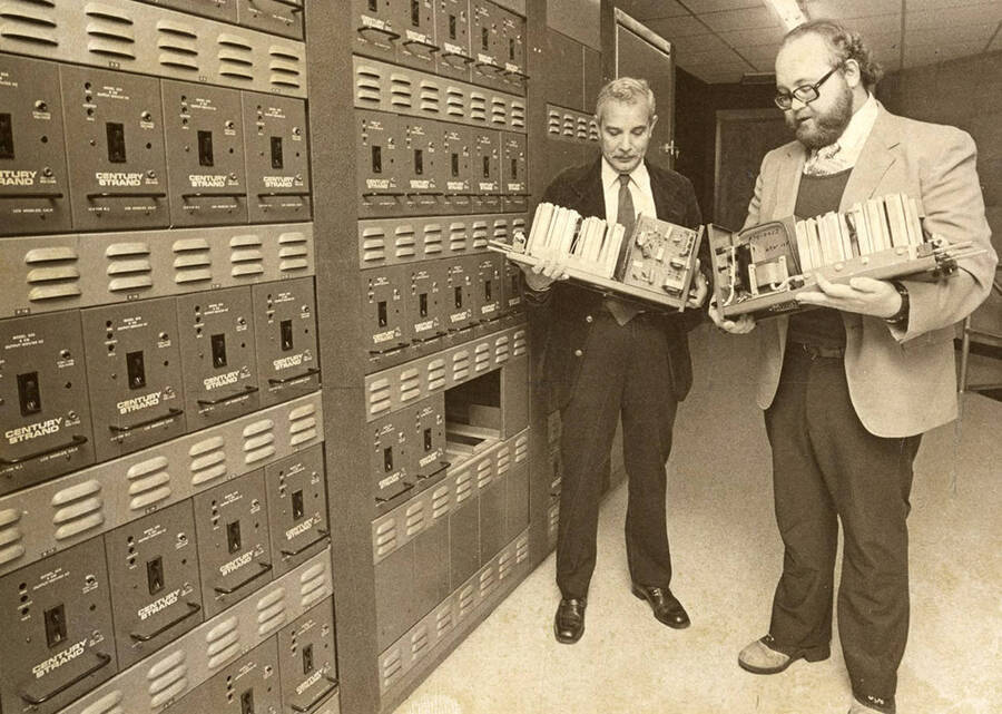 Ed Chavez [Left] and a man examine dimmer packs in the Hartung Theatre. Dimmer packs were part of the Performing Arts Center stage lighting control system.