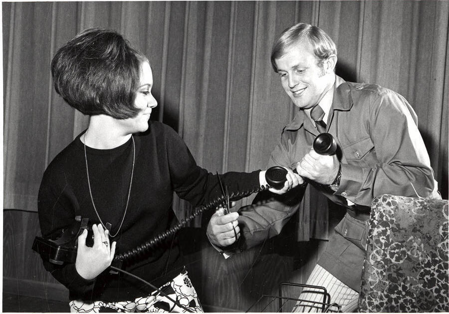 Scene from the University of Idaho production of 'The Telephone.' Two actors can be seen holding a phone, while one of them is cutting the chord with scissors.
