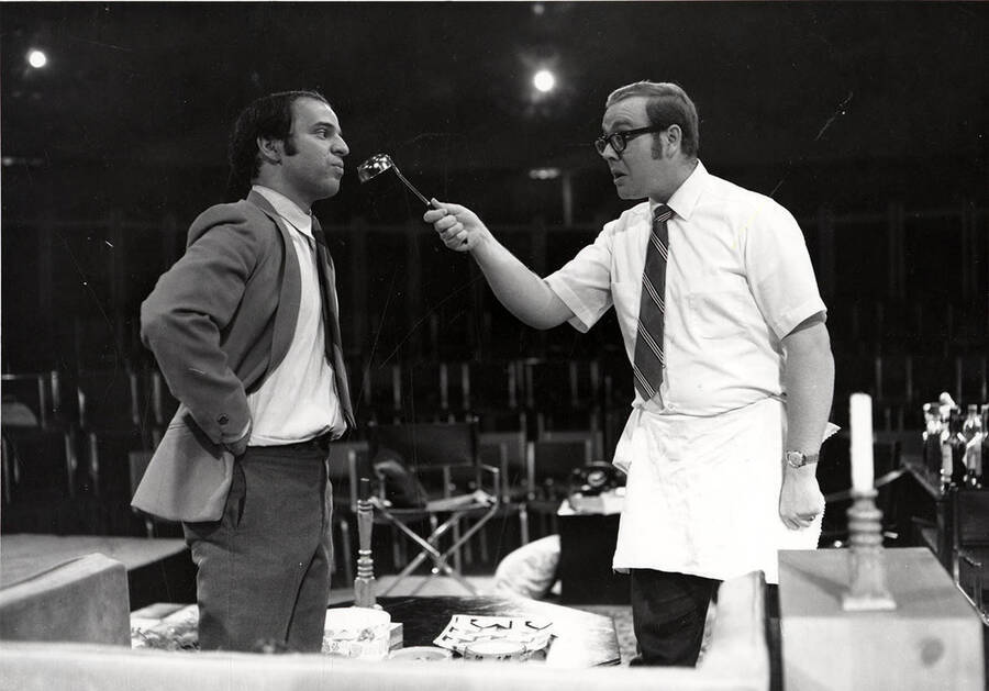 Scene from the University of Idaho drama production of 'The Odd Couple.' This production was directed by Edmund Chavez. A man can be seen holding a ladle up to another man.