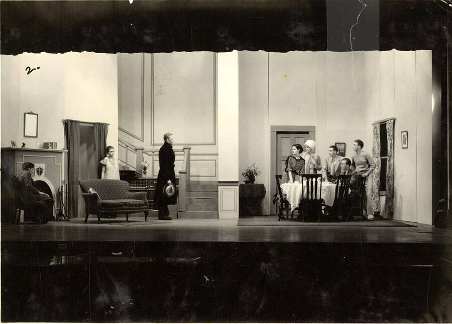 Scene from the University of Idaho drama production of 'Three Cornered Moon.' Many actors can be seen gathered around a table. Cast members include Helen Wilson as Elizabeth Rimplegar, Erma Lewis as Mrs. Eimplegar, Aldrich Bowler as poet, Jean Ricker as Kitty, Burnell Baker as Dr. Stevens, and Catherine Bjornstad as Jenny.