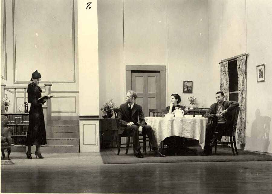 Group scene from the University of Idaho drama production of 'Three Cornered Moon.' Three actors can be seen sitting around a table, conversing with a woman. Cast members include Helen Wilson as Elizabeth Rimplegar, Erma Lewis as Mrs. Eimplegar, Aldrich Bowler as poet, Jean Ricker as Kitty, Burnell Baker as Dr. Stevens, and Catherine Bjornstad as Jenny.