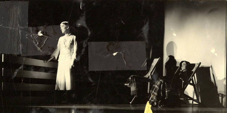 Scene from the University of Idaho drama production of 'Hairy Ape.' One woman can be seen standing on stage, while another sits in a chair, looking on.