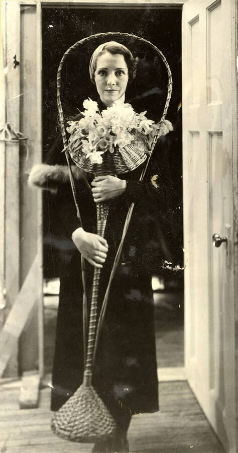Scene from the University of Idaho drama production of 'Torchbearers.' A woman can be seen dressed in costume and holding flowers. Members of the cast include Catherine Brandt as Mrs. J. Duro Pampinelli, Grace Eldridge as Mrs. Nelly Fell, Marthalene Tanner as Mrs. Paula Ritter and Leland Cannon as Fred Ritter.