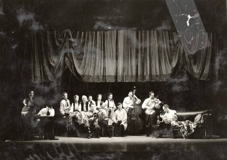 Scene from the University of Idaho drama production of 'The Living Corpse.' Actors can be seen on stage, holding musical instruments. Cast members include Fred C. Blanchard as Fedya, Ethlyn O'Neal as Lisa, Clayne Robison as Victor, Alberta Bergh Utt as Masha, Raphael Gibbs as Prince Sergius, Erma Lewis as Anna Pavlovna, Casady Taylor as Petrovitch, Earl Bopp as Artimiev, and Joe Paquet as Petushkov.