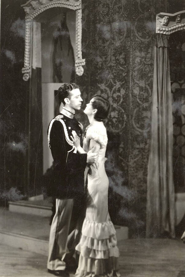Scene from the University of Idaho drama production of 'Death Takes a Holiday.' In this scene, Prince Sirki and Grazia can be seen standing in each other's arms. Members of the cast include Lionel Campbell as Prince Sirki, Bertha Moore as Grazia, Clayne Robison as Duke Lambert, Winfred Janssen as Eric Fenton, Howard Altnow as Corrado, Raphael Gibbs as Baron Cesarea, and Casady Taylor as Major Whitred.