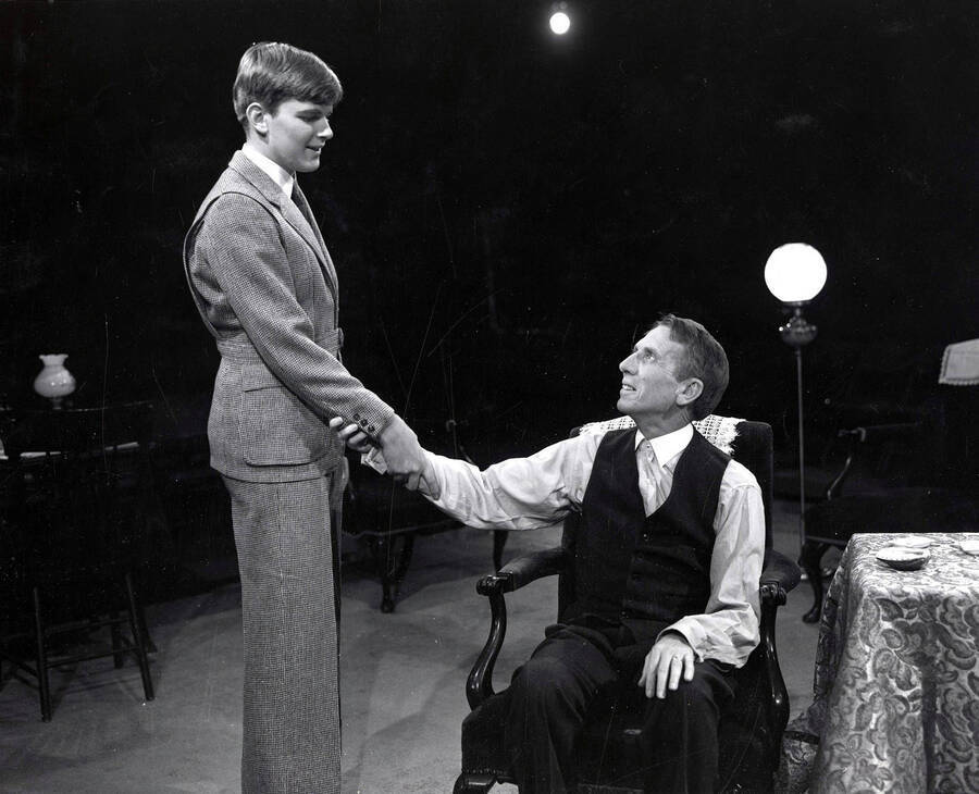 Scene during the University of Idaho drama production of 'Ah, Wilderness.' Bill Byrd (right) is sitting in a chair, shaking the hand of another actor.
