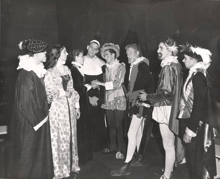 Group scene during the University of Idaho drama production of 'Much Ado About Nothing.' This production was directed by Edmund Chavez. Members of the cast are dressed in costume and all standing around talking with each other.