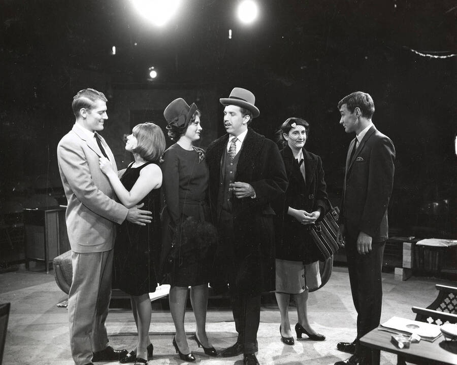 Scene during the University of Idaho drama production of 'Come Blow Your Horn.' A group of people can be seen standing on stage in costume and conversing with each other.