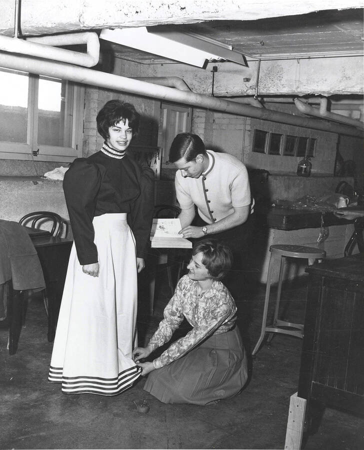 Preparing the wardrobe for the studio production for the University of Idaho drama production of 'Life With Father.' A woman can be seen having her dress tailored backstage.