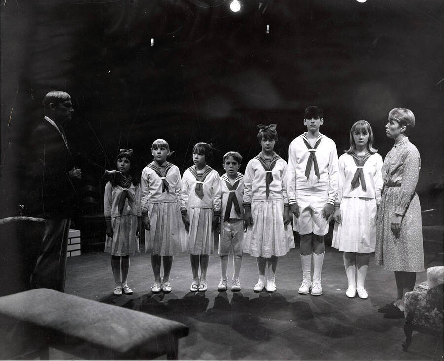 Von Trapp family during the drama production of 'Sound of Music.' This production was directed by Edmund Chavez. Seven children can be seen standing on stage and dressed in matching costumes.
