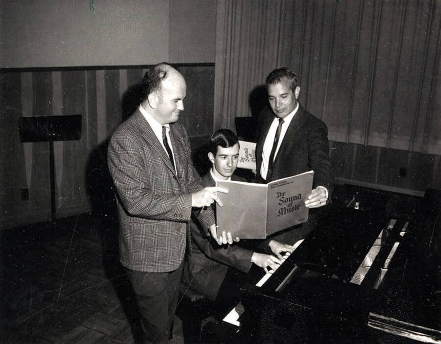 Charlie Walton [Left], Ed Chavez [Right] and another person look at a book titled 'Sound of Music.' One of the men can be seen playing the piano.