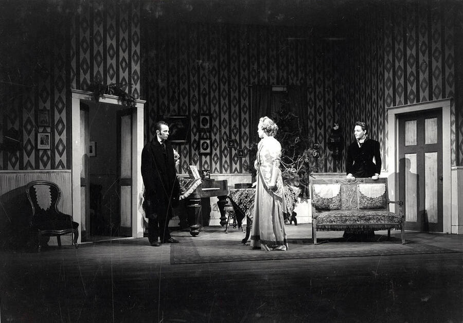 Scene from the University of Idaho drama production of 'A Doll's House.' This production was directed by Jean Collette. Two men and a woman can be seen on stage talking with each other.