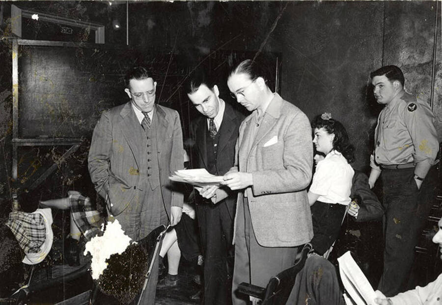 Scene from the University of Idaho drama production of 'Gee-Eyes Right.' A group of men can be seen looking at a document together.