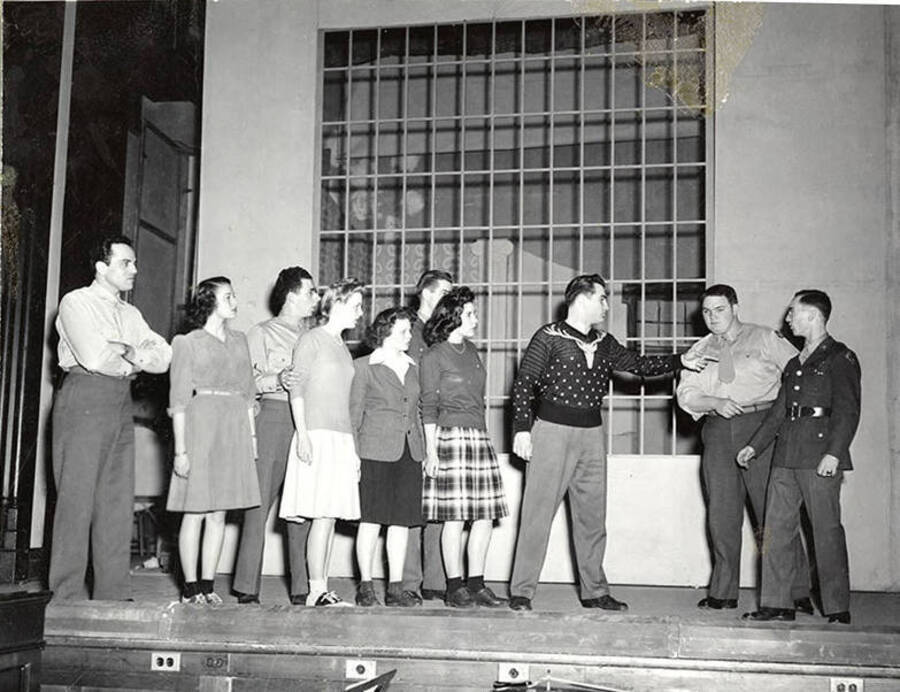 Scene from the University of Idaho drama production of 'Gee-Eyes Right.' One man can be seen pointing at another man, while other members of the cast look on.