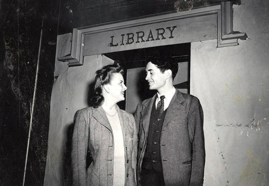 Scene from the University of Idaho drama production of 'Gee-Eyes Right.' A man and a woman can be seen looking at each other, while standing under a sign that reads 'Library'.