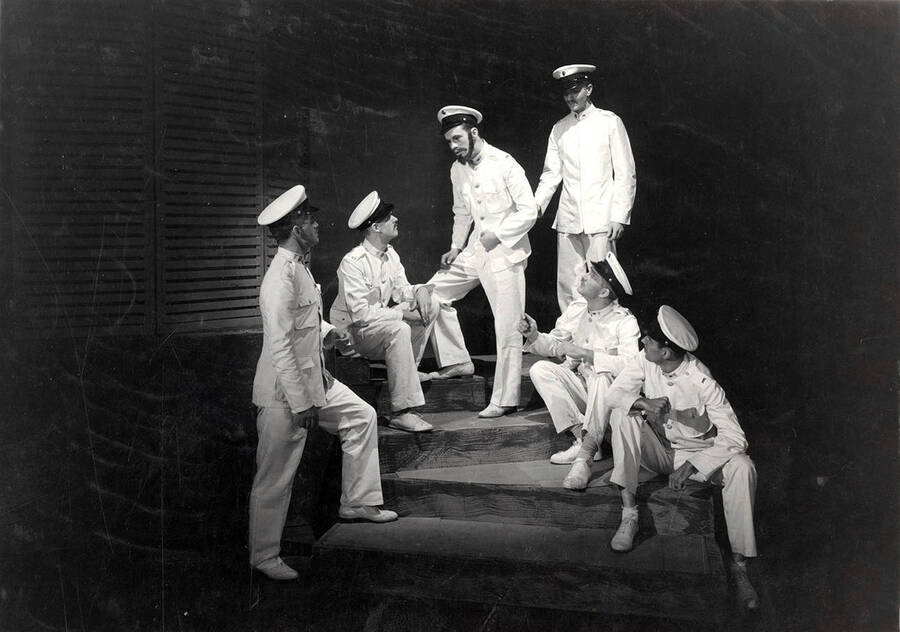 Group scene during the University of Idaho drama production of 'Yellow Jack.' This production was directed by Jean Collette. The men can all be seen dressed alike in white costumes. One man is talking, while the other five listen.