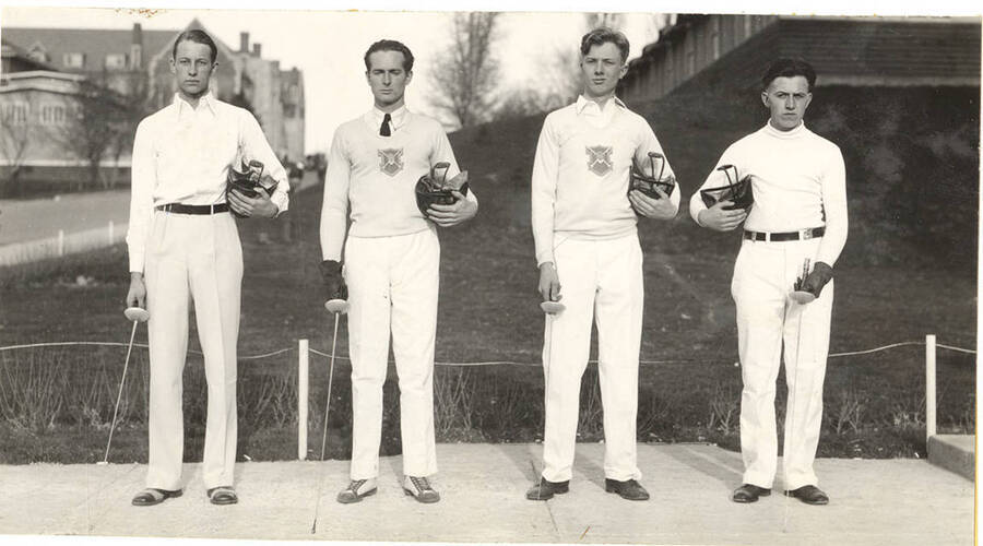 Members of a 1930's men's Fencing varsity club pose beside Memorial Gymnasium for a team photograph.