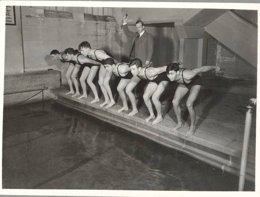 The 1936 men's Swimming team prepares a tandem dive as head coach Bob Tessier presses his finger on the trigger of the starting-shot pistol.