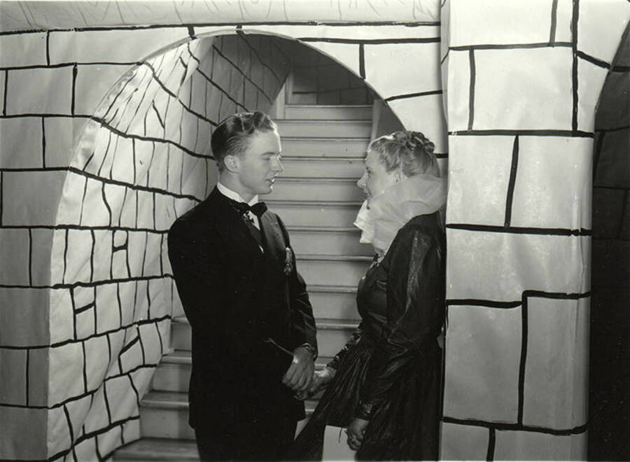 Two people in fairy-tale themed costumes stand next to a brick-patterned paper entrance at the Phi Delta Theta Storybook Ball.