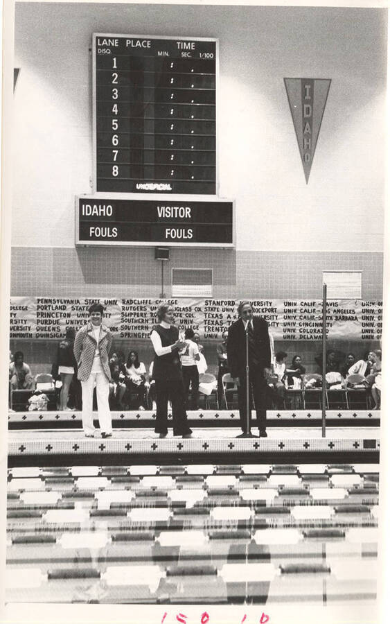 An unidentified speaker talks alongside two Swimming coaches at the opening of the AIAW National Championships in Idaho's Swim Center.