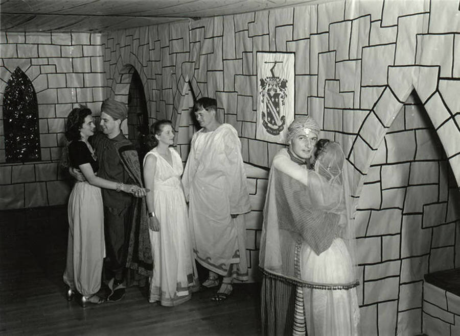 Couples in costumes dance in front of a brick-patterned backdrop at the Storybook Ball.