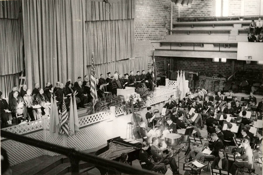 A group of dignitaries sitting on stage while the band are preparing for Commencement. From files of C.J. Brosnan