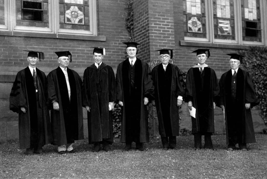 [from l-r] Clency St. Clair, Asher B. Wilson, University of Idaho President Mervin G. Neale, T.A. Waeters, J.J. Day, John W. Condie, and W.D. Vincent standing together outside the Memorial Gym dressed in caps and gowns for Commencement.