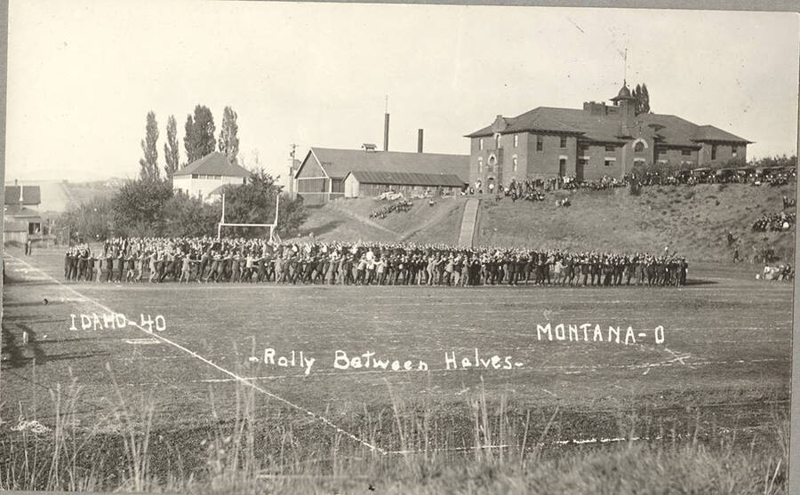 Audience participates in a serpentine on MacLean Field at halftime during a football game. Caption reads: Idaho-40-Rally Between Halves-Montana-0