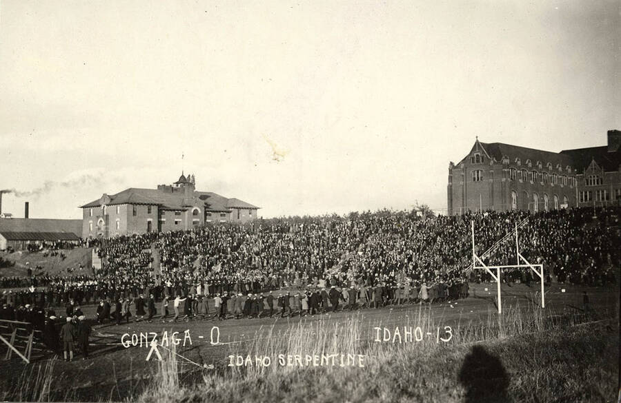 Audience members participate in a serpentine during a football game. Caption reads: Gonzaga-0 Idaho-13, Idaho Serpentine.