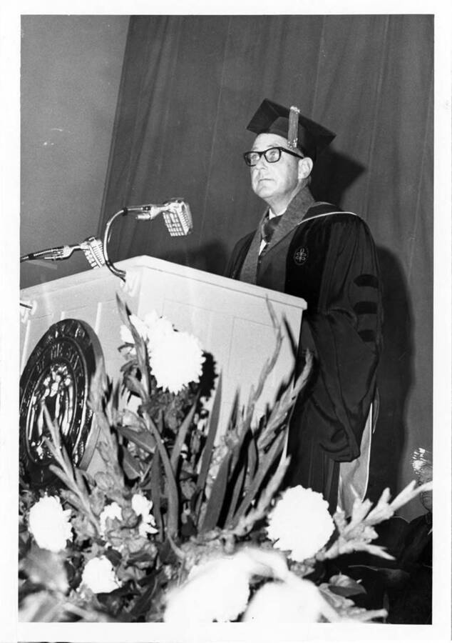 Commencement speaker, University of Idaho President Ernest W. Hartung, delivers his address from a podium during the 1966 Commencement ceremony. Photographer Publications Department