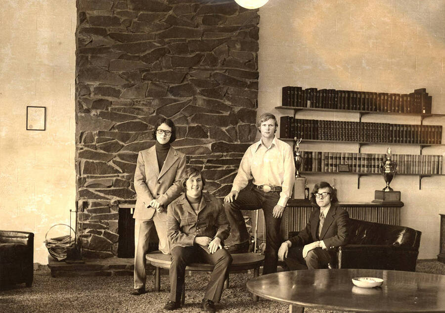 A group photograph of the Sigma Chi officers for the academic year 1972-1973, taken in the living area. Individuals pictured: Robert M. Pickett, president; Raymond G. Stark, vice president; H. Thomas Vanderford, treasurer; Quinton A. Snook, secretary.