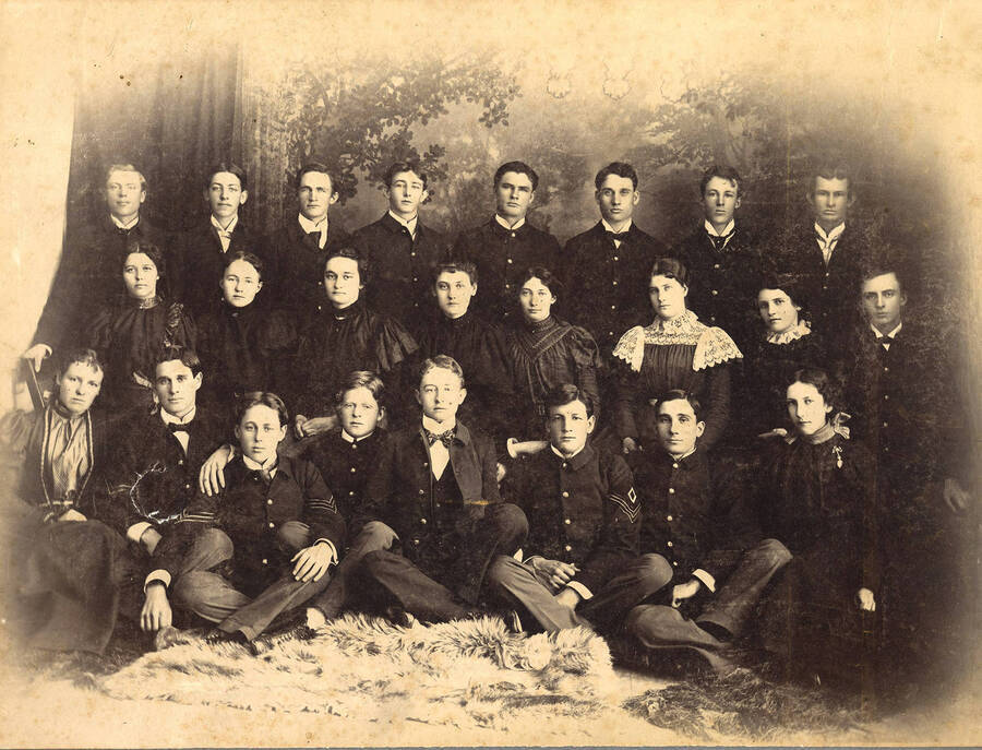The graduating class of 1901 poses together for a formal portrait in a photography studio. Individuals identified on mount.