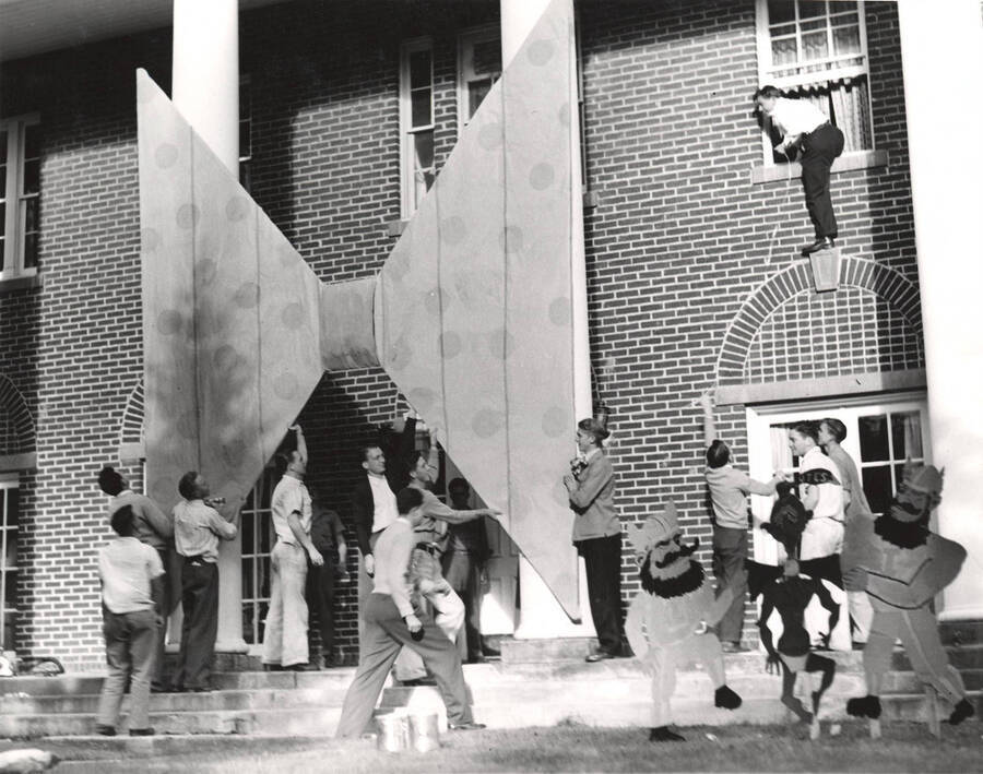 Members of Kappa Sigma help each other hang a bowtie above the entrance to the Kappa Sigma house.
