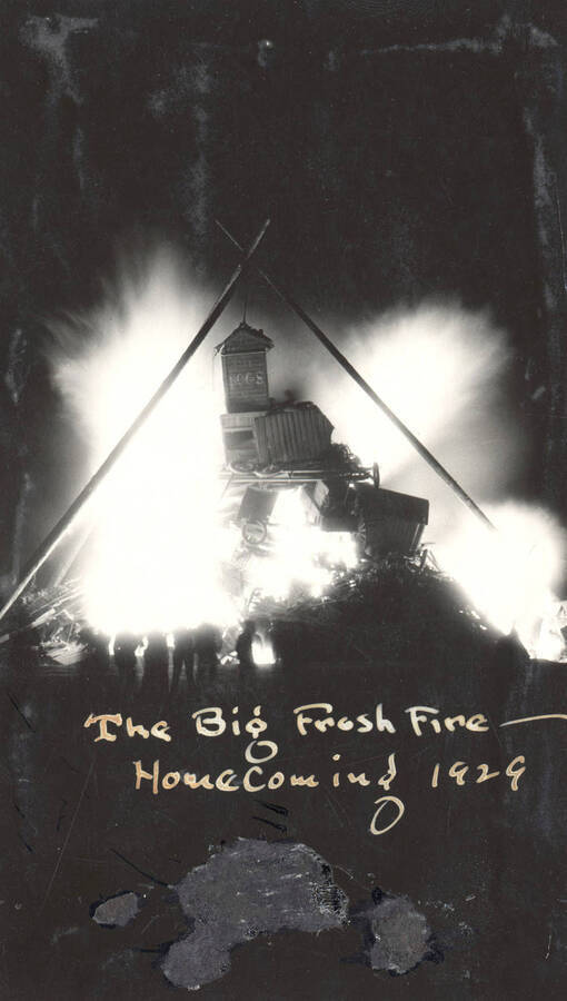 Spectators watch as the Homecoming Freshman bonfire burns in the background. The caption on the photograph reads: 'The big frosh fire- Homecoming 1929'.