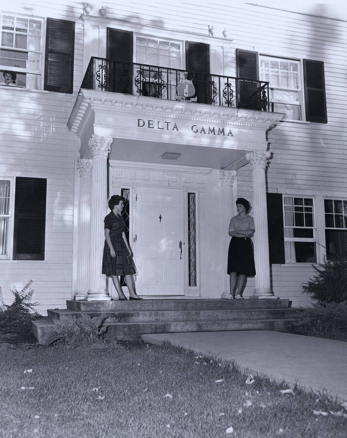 Girls standing by doorway of Delta Gamma house, which is on the northeast corner of Idaho and Elm Streets.
