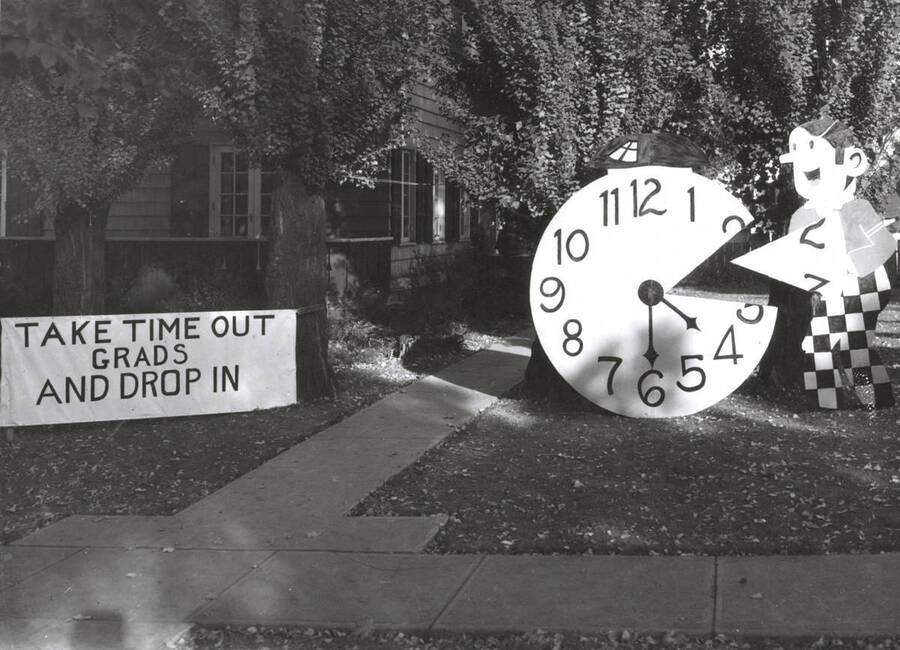 Alpha Chi Omega's house decorations depict a sign that reads 'Take Time Out Grads and Drop In'. A cutout of a clock with a slice taken out of it like a pizza accompanies the sign.
