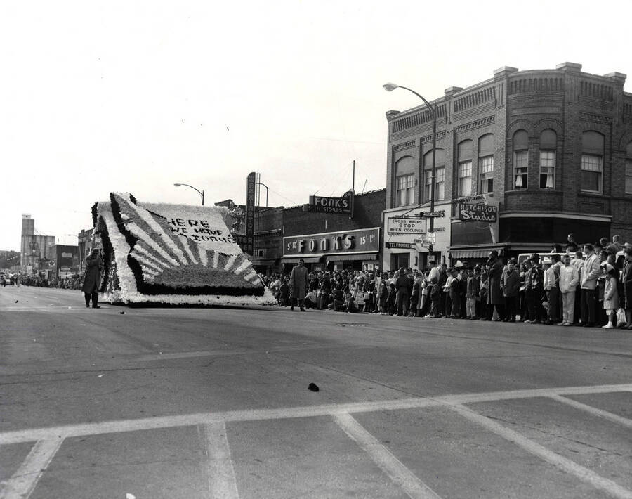 Float during the Homecoming parade showcasing the State of Idaho, caption reads "Here We Have Idaho".