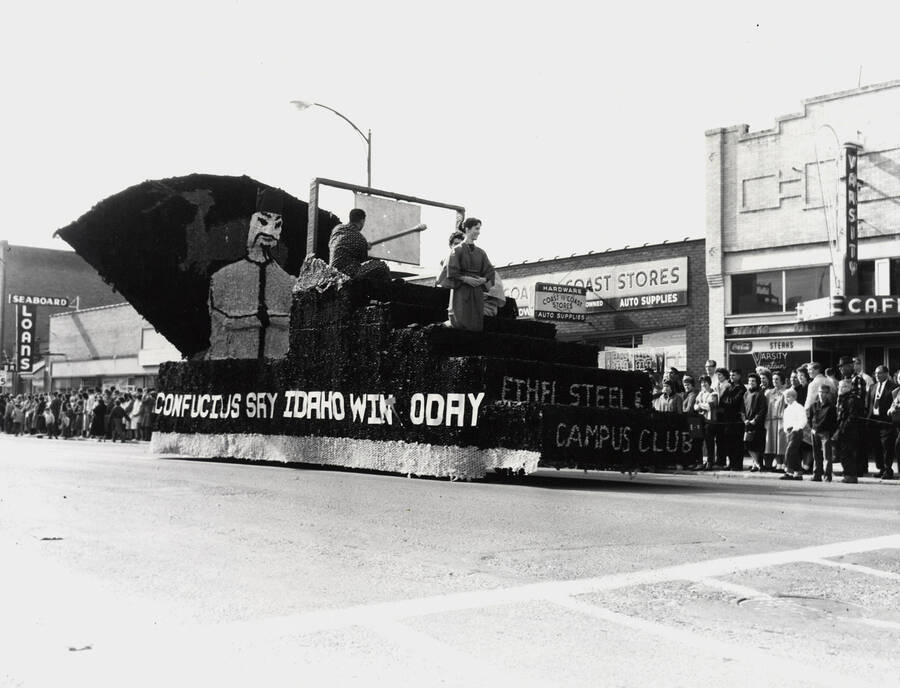 An unidentified float in front of Seaboard Loans, Coast to Coast, and Varsity Cafe during the Homecoming parade. The side of the float reads 'Confucius Say, Idaho Win Today'.