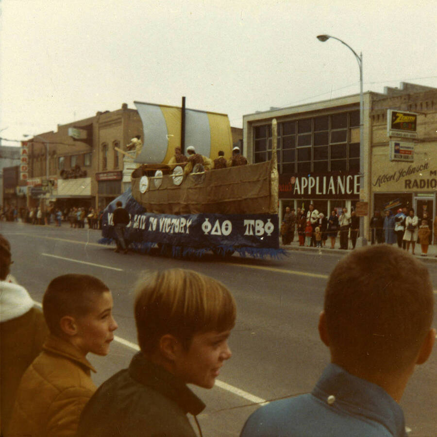 A color photo of the Pi Beta Phi and Phi Delta Theta Viking themed float and spectators during of the Homecoming parade.